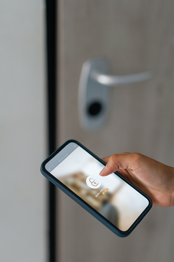 Close-up on a woman locking the door of her house using an app on her cell phone - smart home technology. **DESIGN ON SCREEN WAS MADE FROM SCRATCH BY US**