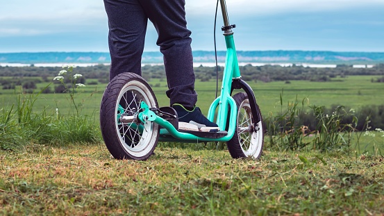 Child's feet on a scooter with large wheels among the green grass. Active lifestyle