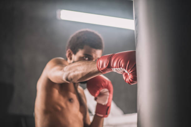 Dark-skinned kickboxer having a workout in a gym and looking involved Workout. Dark-skinned kickboxer having a workout in a gym and looking involved boxing gym stock pictures, royalty-free photos & images