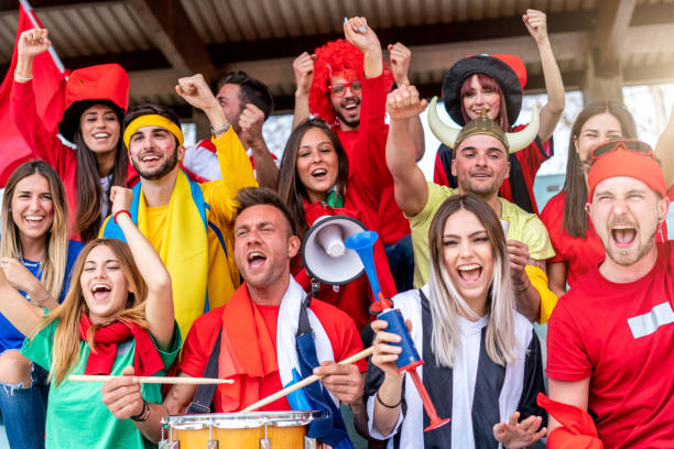 istock Multi colored fans at stadium are supporting their team 1325948622