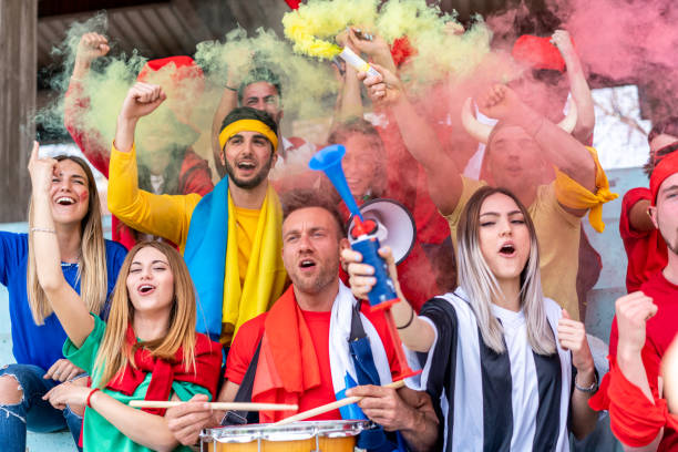 istock Multi colored fans at stadium are supporting their team 1325948624
