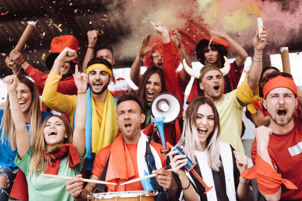 istock Multi colored fans at stadium are supporting their team 1325948628