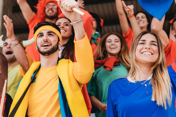 istock Multi colored fans at stadium are supporting their team 1325948631