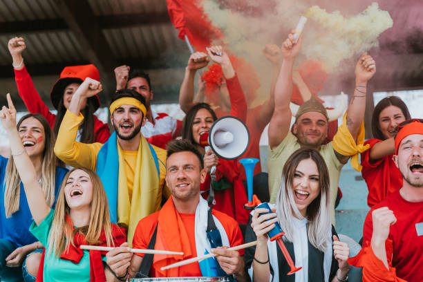 istock Multi colored fans at stadium are supporting their team 1325948635