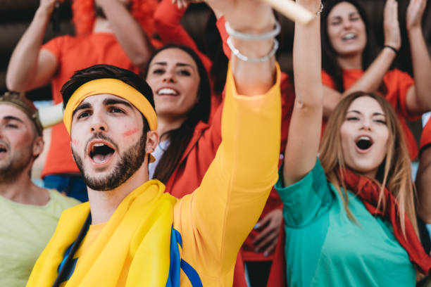 istock Multi colored fans at stadium are supporting their team 1325948639