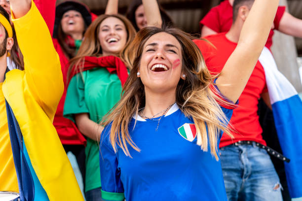 istock Multi colored fans at stadium are supporting their team 1325948643