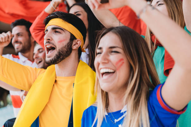istock Multi colored fans at stadium are supporting their team 1325948645