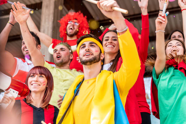 istock Multi colored fans at stadium are supporting their team 1325948653