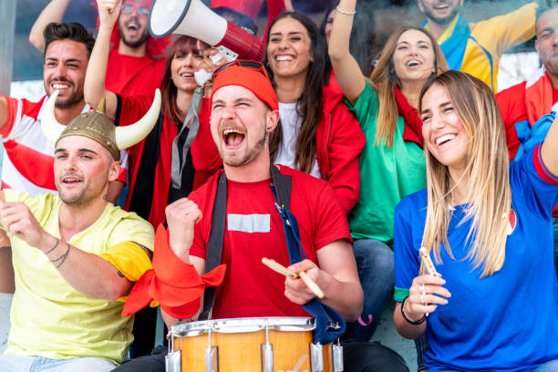 istock Multi colored fans at stadium are supporting their team 1325948654