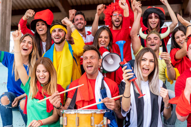 istock Multi colored fans at stadium are supporting their team 1325948655