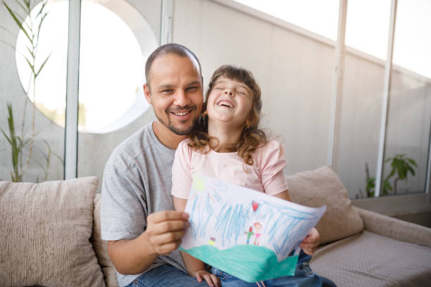행복한 아버지와 딸이 카메라에 그녀의 집에서 만든 카드를 보여주는 - fathers day greeting card father child 뉴스 사진 이미지