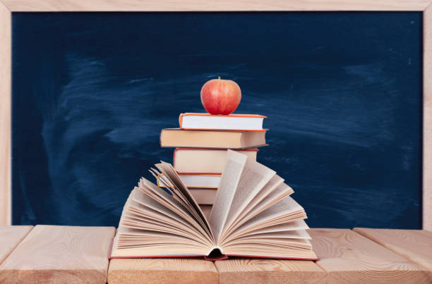 istock Open book on the wood table with stack of books and red apple on the class board background 1325954828