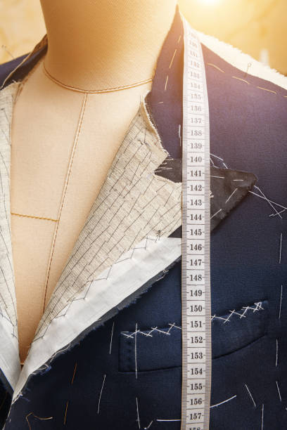 istock Semi-ready jacket on mannequin with measuring tape across neck. Suit tailoring in process of custom-made jacket. Bespoke suit tailoring in tailor workshop. Working on a made-to-measure suit jacket 1325957916