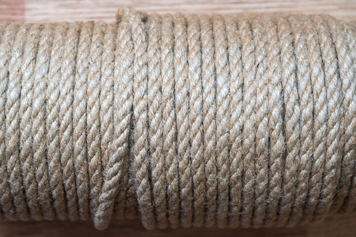 A twisted rope made of natural material is wound on a bobbin. Side view. Jute fibers are visible. Background. Texture.