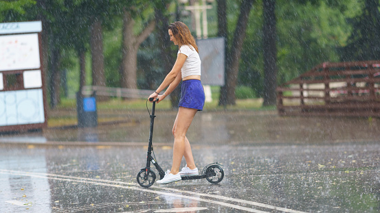 Moscow, Russia. June 27, 2021: Raining day in city at summer. Wet two young women riding motor scooter. Texture of strong, fresh and powerful water sprays. Tropical storm as result of global warming