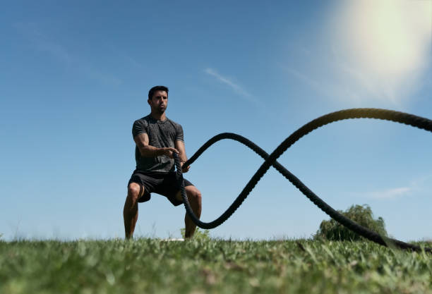 Male athlete on the outdoor in the park, exercises for endurance, using a thick rope, for cross fitness. European In summer stock photo