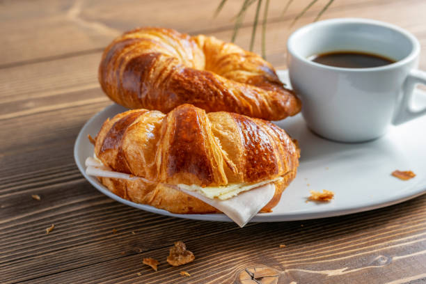 Two French croissants with ham and cheese and a cup of black coffee on the white plate. Wooden table, morning country breakfast.Side view at an angle. Two French croissants with ham and cheese and a cup of black coffee on the white plate. Wooden table, morning country breakfast. Side view at an angle. cafe sandwich stock pictures, royalty-free photos & images