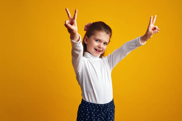 istock Girl showing peace gesture with both raised hands against yellow background 1325964491