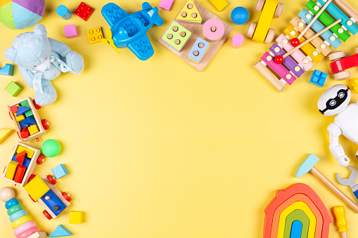 Colorful educational wooden plastic and fluffy toys for children on yellow background. Top view, flat lay