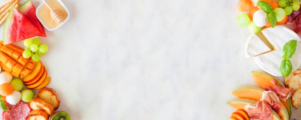 istock Summer fruit theme charcuterie double border against a white marble background 1325972101
