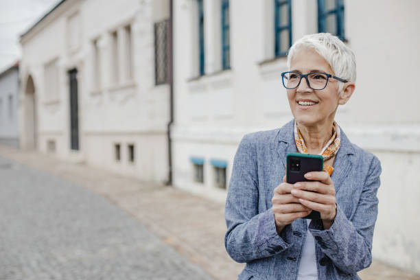 istock Senior woman is using mobile phone on the street 1325973812