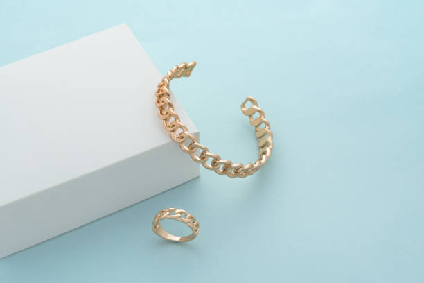 istock Chain shape gold bracelet and ring on white box on blue background with copy space 1325975977