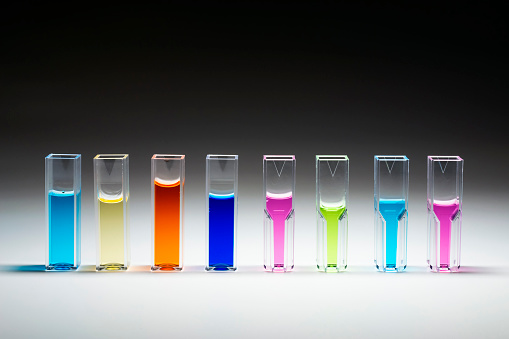 Quartz or polymer Cuvettes for photometric analysis in analytical chemistry filled with liquids of different colors on the gradient white to black background.