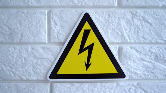 Electricity danger a sign on yellow background. A danger sign hangs on a wall. 4k stock footage.