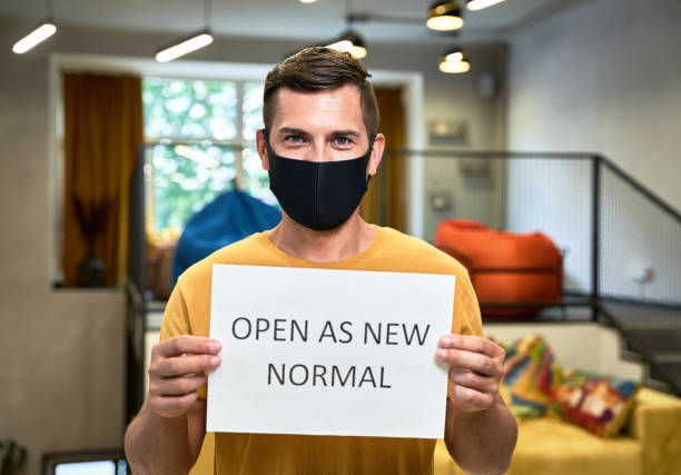 istock Man in mask holds paper with text Open As New Normal in office 1325979801