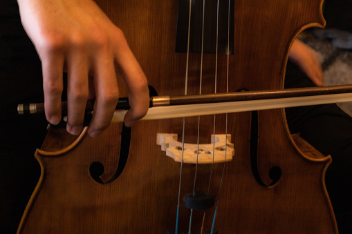detail of a hand holding a music bow to play a cello and to bring out the sound with selective focus