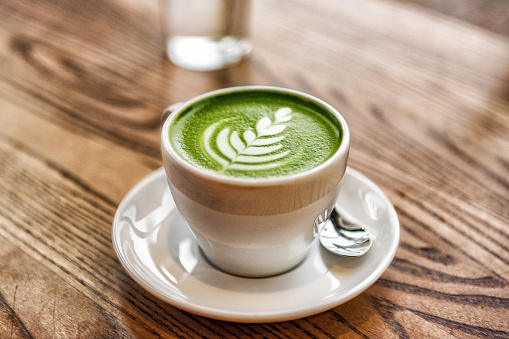 Matcha latte green milk foam cup on wood table at cafe. Trendy powered tea trend from Japan