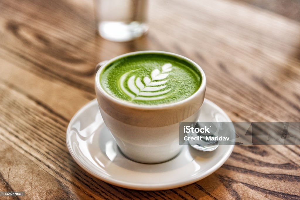 Matcha latte green milk foam cup on wood table at cafe. Trendy powered tea trend from Japan Matcha latte green milk foam cup on wood table at cafe. Trendy powered tea trend from Japan. Matcha Tea Stock Photo