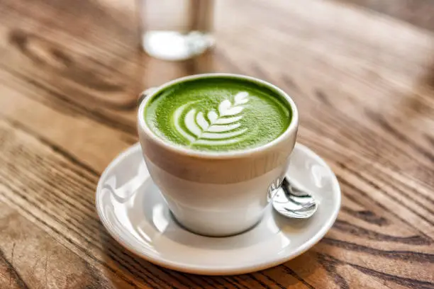 Matcha latte green milk foam cup on wood table at cafe. Trendy powered tea trend from Japan.