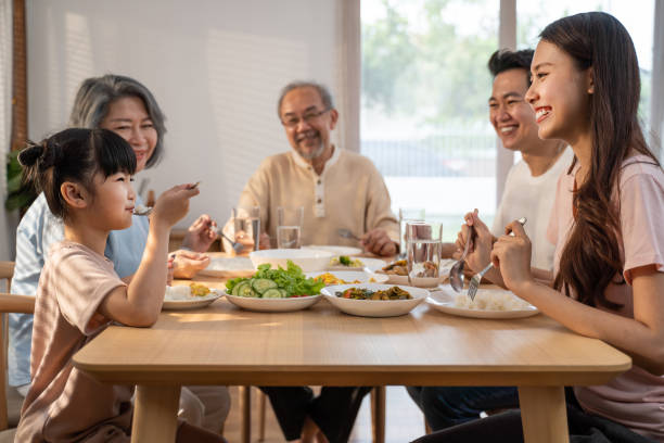 big asian happy family spend time having lunch on dinner table together. little kid daughter enjoy eating food with father, mother and grandparents. multi-generation relationship and activity in house - 1474 imagens e fotografias de stock