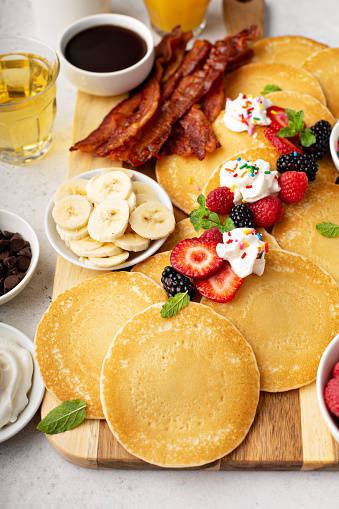 Big pancake breakfast table with berries, bacon and maple syrup