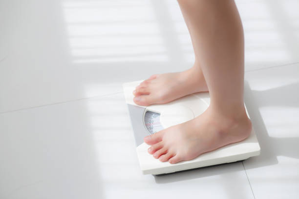 Lifestyle activity with leg of woman stand measuring weight scale for diet with barefoot, closeup foot of girl slim weight loss measure for food control and nutrition, healthy care and wellness concept. stock photo