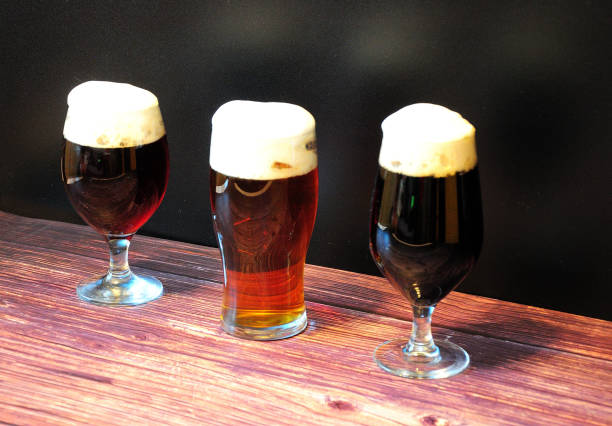 trzy różne szklanki z jedną trzecią różnych rodzajów ciemnego piwa są w rzędzie na drewnianym stole. - draught beer variation three objects zdjęcia i obrazy z banku zdjęć