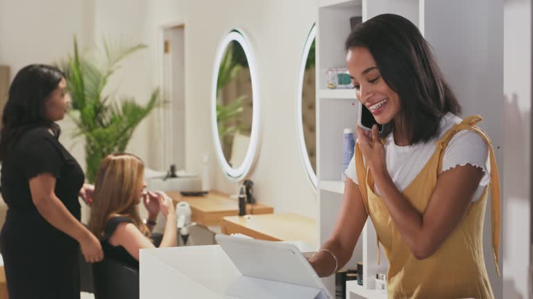 4k video footage of an attractive young woman standing in her salon and using technology to book appointments