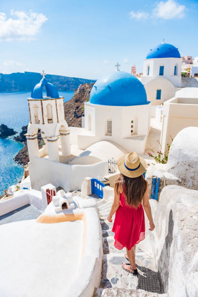 viaje europa chica turista caminando en las escaleras de santorini de las calles de la ciudad, famoso destino europeo tres cúpulas azules, famoso punto de referencia griego. pueblo de oia, isla de santorini, vacaciones de lujo - travel locations cyclades islands santorini vertical fotografías e imágenes de stock