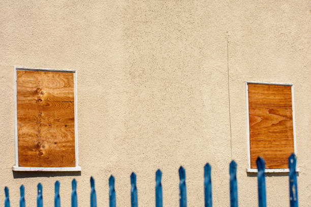 two small windows boarded up with plywood sheet - cyclone fence imagens e fotografias de stock