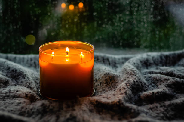 Burning aroma candle puts on table near by window that have rain drop