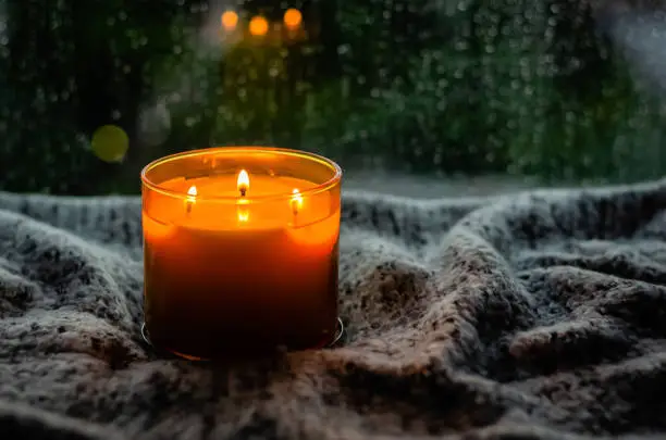 Photo of Burning aroma candle puts on table near by window that have rain drop