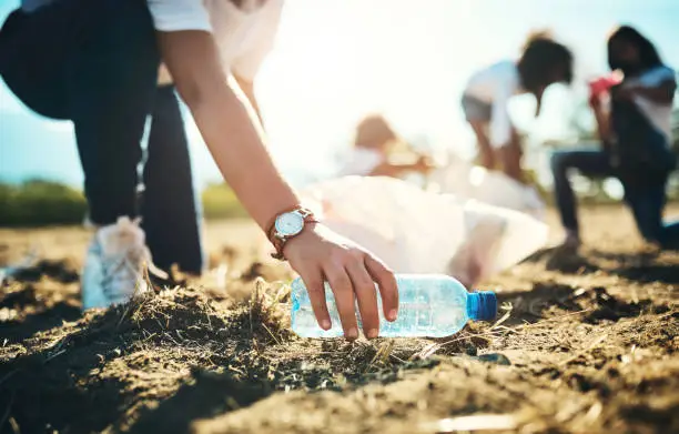 Photo of Shot of an unrecognisable teenager picking up litter off a field at summer camp