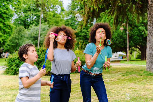 African-American Family is Spending the Time Together in a Public Park and Blowing Bubbles.