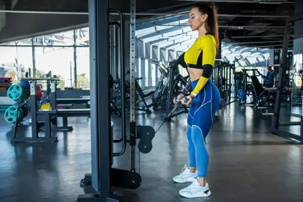 Photo of Sporty girl doing biceps curl on cable crossover at gym