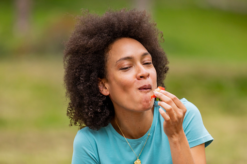 A Young Woman of African-American Ethnicity is Enjoying in Walking Through the Park and Eating Fresh Strawberries.