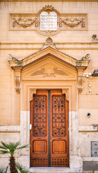 The main door of the Jewish synagogue and school of the Castro Oratory, in the heart of the Monti district of Rome. This Jewish temple, built in 1914 by the same architects who built the Synagogue of the Tempio Maggiore in the Roman Ghetto, reflects the Art Nouveau style of the early twentieth century. The Monti district is a popular and multi-ethnic quarter much loved by the younger generations and tourists for the presence of trendy pubs, shops and restaurants, where you can find the true soul of the Eternal City. The quarter, located between the Esquiline Hill and the Roman Forum, is also rich in numerous churches and archaeological remains from the Roman era. Image in high definition format.