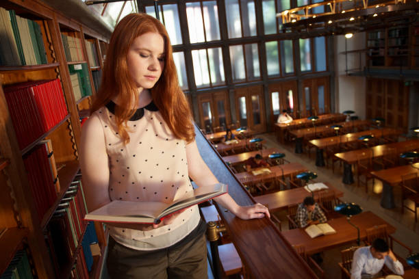 istock Young woman reading a book in public library 1326028217