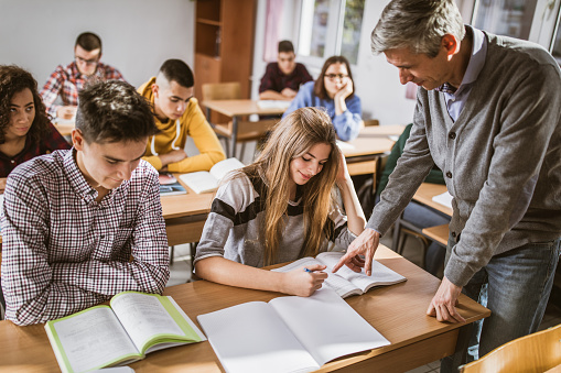 Mid adult teacher assisting his students on a class at high school. Focus is on woman.