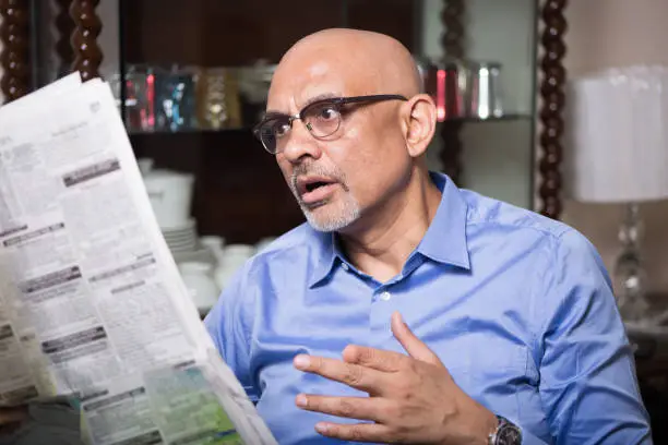 Mature man at home in shock expression while reading breaking news in the newspaper